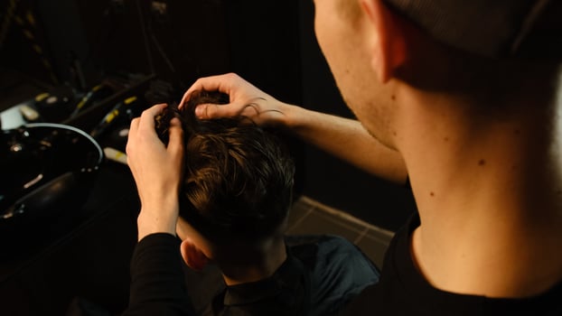 Barber shop. Man in barber's chair, hairdresser styling his hair with hands in dark key lightning. Hairdresser for man photo