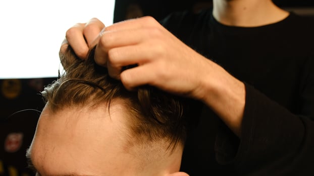 Barber shop. Man in barber's chair, hairdresser styling his hair with hands in dark key lightning. Hairdresser for man photo