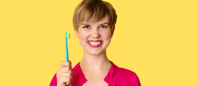 A smiling woman with healthy teeth holds a toothbrush in her hands. A young beautiful girl on a bright background. Oral hygiene. A place for your text. photo