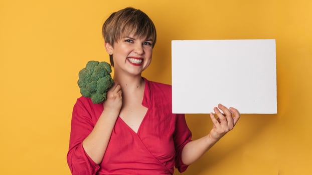 A studio shot of a young smiling woman holding fresh broccoli and a blank letterhead. The concept of healthy eating. A place for your text. Panoramic banner. photo