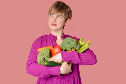 Studio shot, a young Caucasian woman holding a lot of fresh vegetables in her hands. The concept of healthy eating. Vegetarianism. photo