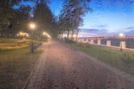 Defocused night park with lanterns behind rainy, wet glass at night. Concept of rainy autumn weather. photo