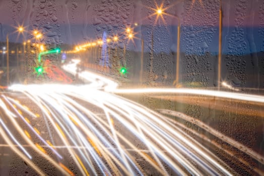 Defocused headlights from moving cars behind rainy, wet glass at night. oncept of rainy autumn weather. photo