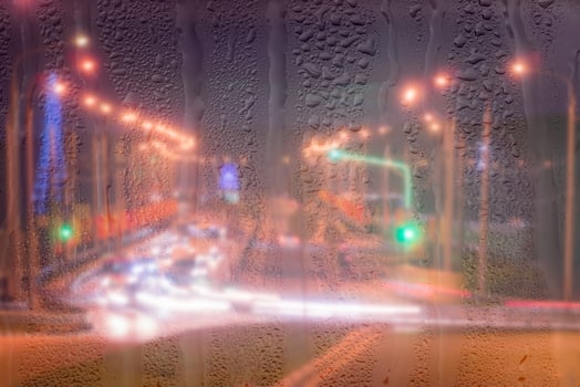 Defocused headlights from moving cars behind rainy, wet glass at night. oncept of rainy autumn weather. photo