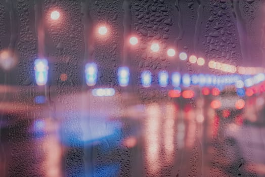 Blurry lights of moving cars and lanterns reflecting on the wet asphalt in the night city behind rain-covered window. photo