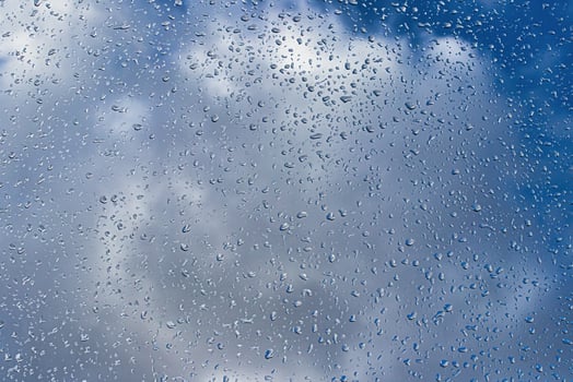 Rain drops on window glasses surface with blue sky and clouds background. Raindrops on a glass. The concept of changing from rainy to sunny weather. photo