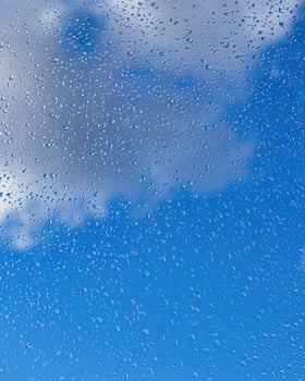 Rain drops on window glasses surface with blue sky and clouds background. Raindrops on a glass. The concept of changing from rainy to sunny weather. photo