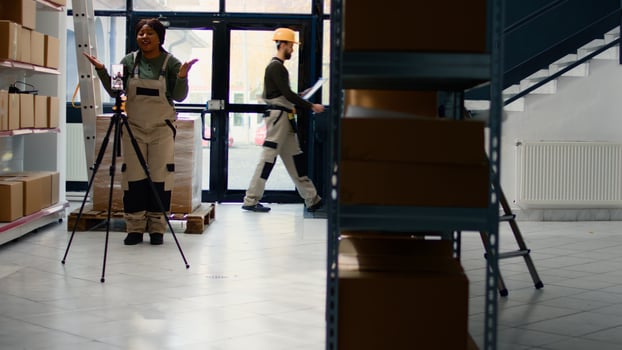 Warehouse marketing executive using smartphone placed on tripod to make for social media platforms. African american advertising specialist films herself in storage hub showcasing her business photo