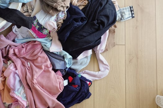 Clothes pile next to laundry basket filled with garments, on hardwood floor photo