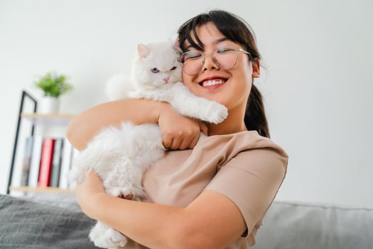 A woman is holding a white cat and smiling in the living room at home. photo