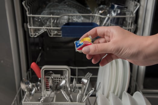 Woman putting detergen kapsul into open dishwasher photo