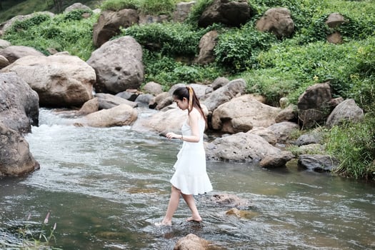 Smiling Beautiful asian female in white dress is standing on the rock and stream in the tropical forest. photo