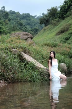 Beautiful asian female in white dress is standing in the stream of tropical forest. photo
