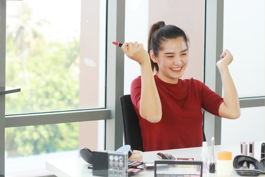 Beautiful Asian woman blogger smiling and hand holding red Lipstick for make up tutorial in Cosmetics website. Marketing in social media concept. photo