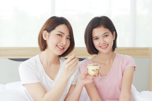 Asian young sisters lovely couple on white bed hand holding cup of cake and eating Bakery together in bedroom. Homosexual women or Lesbian in love. LGBT Asian and Holiday concept. photo