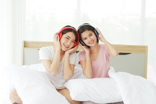 Asian young sisters lovely couple on white listen to music with Headphones and dancing together in bedroom. Homosexual women or Lesbian in love. Music and Holiday concept. photo