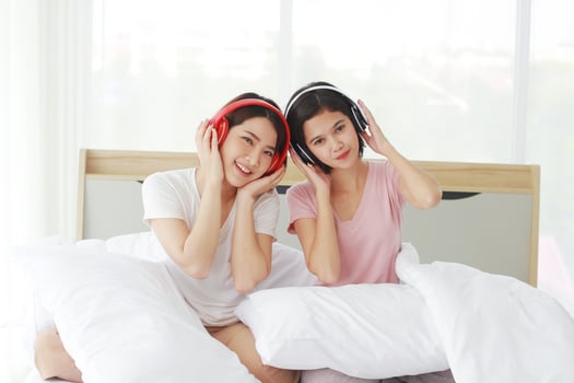 Asian young sisters lovely couple on white listen to music with Headphones and dancing together in bedroom. Homosexual women or Lesbian in love. Music and Holiday concept. photo