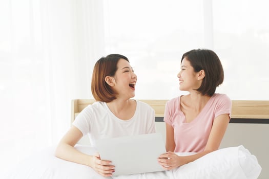 Asian young sisters lovely couple sitting on white bed and smiling together for online Social with laptop in bedroom. Homosexual women or Lesbian in love. LGBT Asian and Holiday concept. photo