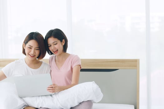 Asian young sisters lovely couple sitting on white bed and smiling together for online social with laptop in bedroom. Homosexual women or Lesbian in love. LGBT Asian and Valentine's Day concept. photo
