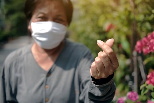Asian old woman wearing white cloth mask for prevent the Covid-19 or Corona virus in Thailand and hand form mini Heart for protection of Air Pollution. Health of elderly concept. Closed up on fingers. photo
