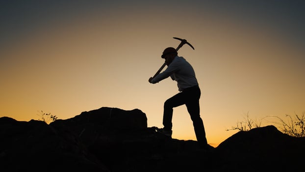 Silhouette Man In Helmet With Pickaxe In His Hands Stands On Rock And Hits Stone photo