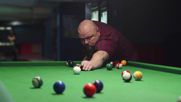 A Big Bald Brutal Bearded Man Plays Billiards On A Green Table, Takes Aim And photo