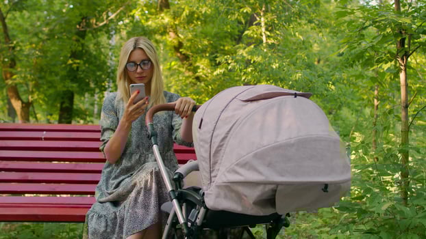 A Young Mother In A Summer Dress Is Sitting On A Red Bench Looking At The Phone photo