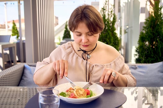 medium sized woman in peach fuzz dress eating cottage cheese pancakes with salmon and spinach in modern restaurant photo