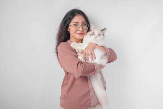 Lovely Asian woman wearing eyeglasses holding her ragdoll cat and smiling to the camera isolated over white background. photo