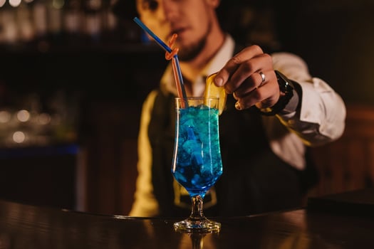 bartender serves a cocktail Blue Lagoon in a glass with a straw at bar counter photo