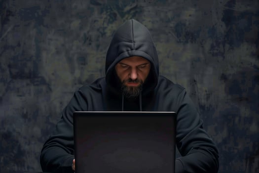 Man in a hoodie sitting at a table with a laptop photo