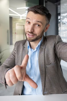 A professional middle-aged man participates in a call, gesturing while conversing. He is in a stylish, contemporary office setting, wearing a suit and a friendly expression. photo