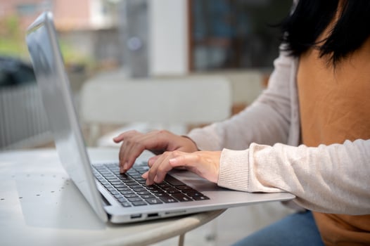 A cropped image of a woman types on her laptop keyboard, and works remotely at an outdoor table. photo