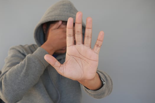 sad man in hood cover face with hands isolated in black. photo