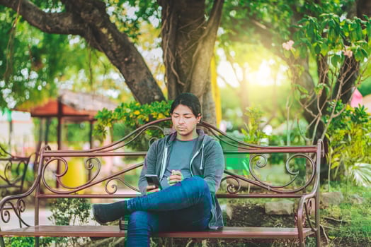 Handsome man sitting on a bench checking cell phone at sunset. Young man sitting on a park bench texting on cell phone photo