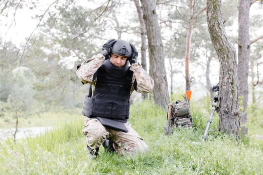 A man in a military uniform and a bulletproof vest works in the forest to demine the territory. A man puts on a protective helmet before starting work photo