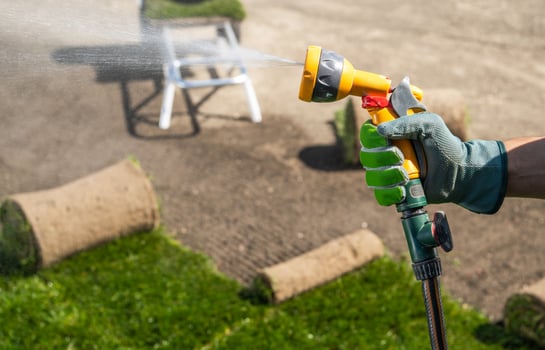 Gardener Spraying Grass Turfs With Water Hose photo