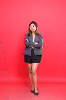 Elegant asian girl executive in gray suit with long hair, white skin, taking photo in studio on red background standing with arms crossed. for corporate concepts, fashion and advertising