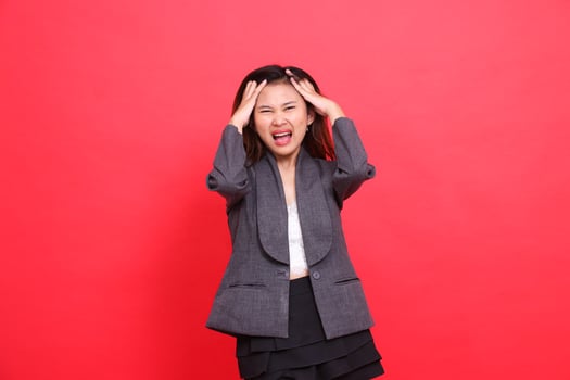 indonesia office woman's expression, severe pain, headache, both hands holding the camera, wearing a gray jacket and red skirt. for health, business and advertising concepts photo