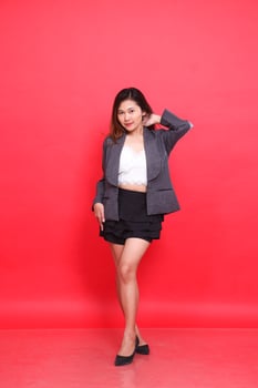 full body asian woman in gray suit looking at camera holding back neck long hair, white skin in studio on red background. for corporate concepts, fashion and advertising photo