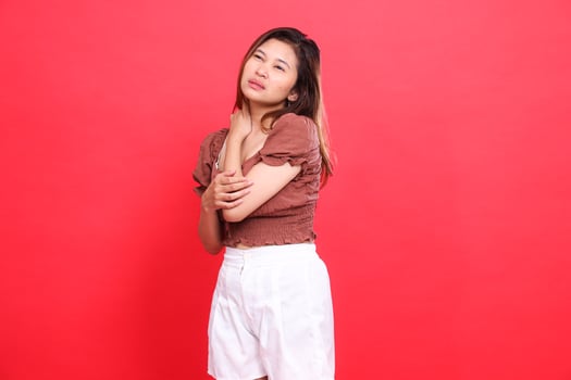 Expression of an indonesia woman with sore shoulders candidly wearing a brown blouse top and shorts on a red background. for health, lifestyle and advertising concepts photo