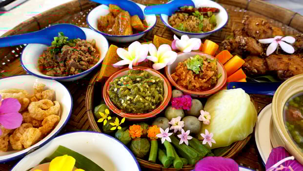 Northern Thai cuisine food set. Pork curry, chilli dip, minced pork salad, soft boiled vegetables and pork snack served in brass dishes. Decorated with flower, garland, spoon and basket background photo