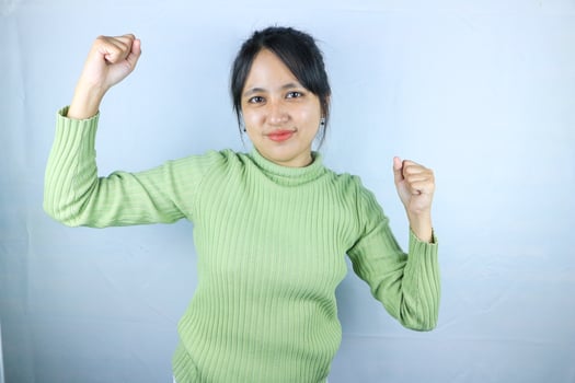 Beautiful Asian woman in a green sweater clenched fists, celebrating victory expressing success photo