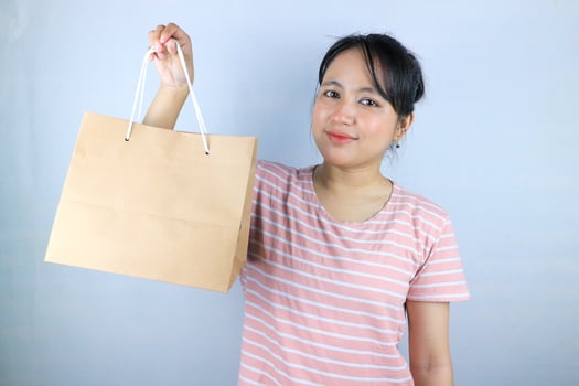 Smiling expression of Asian woman holding craft paper shopping bags on white background photo