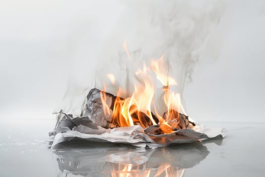 Burning paper engulfed in flames against a transparent white surface, symbolizing destruction and transformation photo