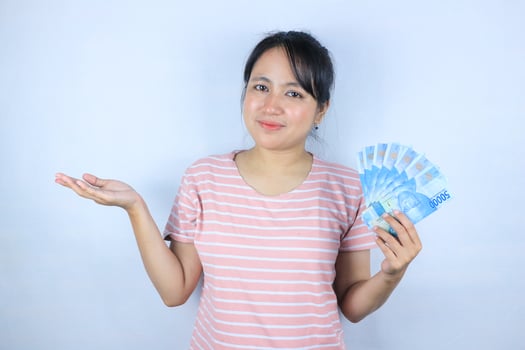 Portrait of a young asian woman holding cash money while showing empty space. Advertisement concept photo