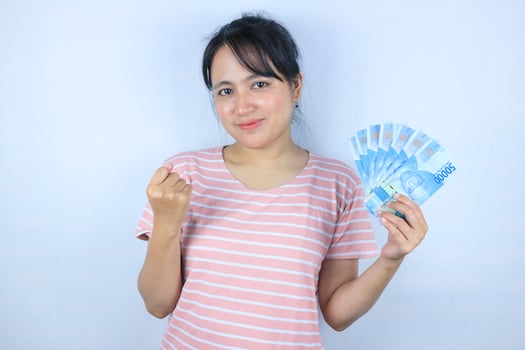 Portrait of a smiling asian young woman holding cash rupiah and celebrating on white background photo