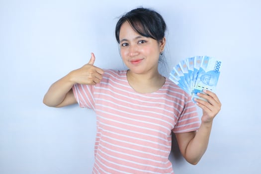 Portrait of a young Asian woman holding cash while giving a thumbs up. Advertising concept photo