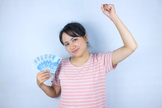 Portrait of a smiling asian young woman holding cash rupiah and celebrating on white background photo