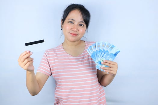 Portrait of a smiling asian young woman holding cash rupiah and credit card on white background photo